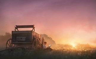 LDS art picture of Joseph Smith resting against the wagon reading the Bible at sunrise. 