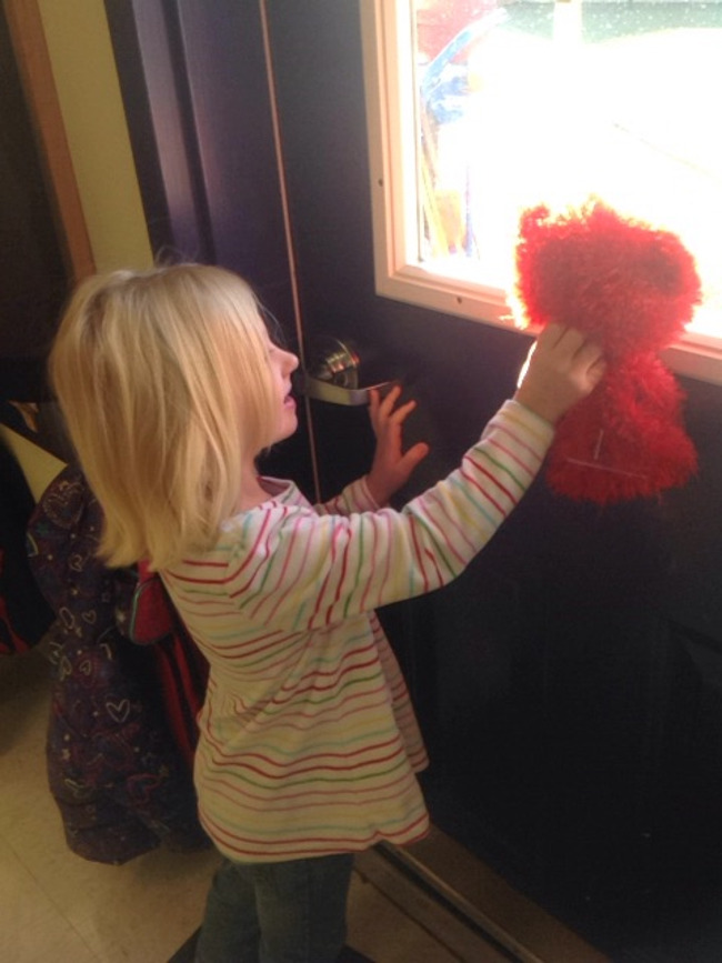 Young Primrose student holds up Benjamin the bear hand puppet up to the window