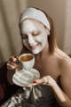 Woman holding a coffee cup with a face mask on to get dewy skin and relax
