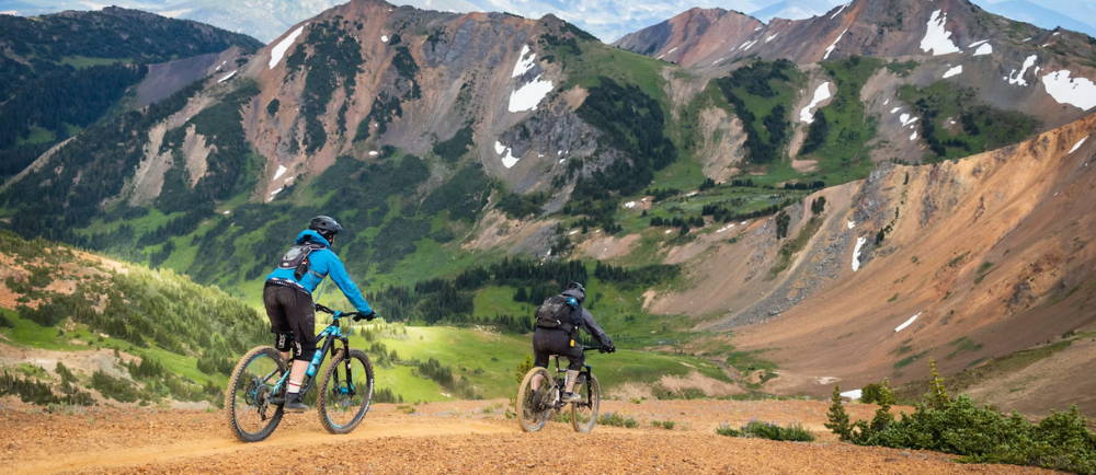 two men riding a trail with mountains in the background