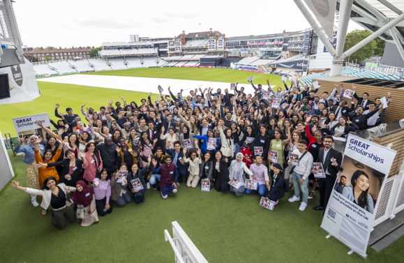 A group photo with people wearing lots of colours of clothing waving and standing in front of The Kia Oval. There is a GREAT Scholarships banner on the left and the right and we can see the cricket ground in the background.