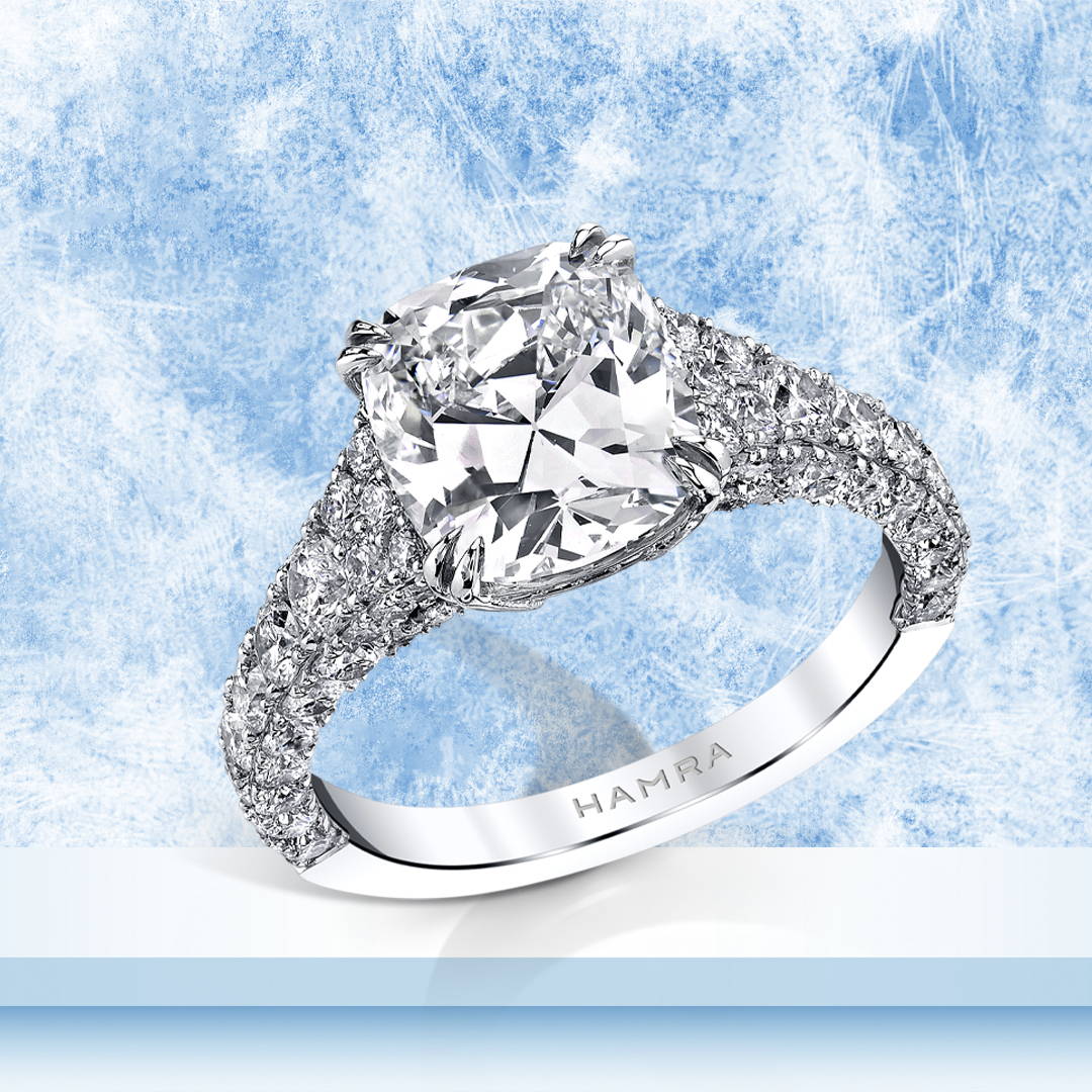 Cushion cut diamond ring with diamond accents in platinum on a blue background.