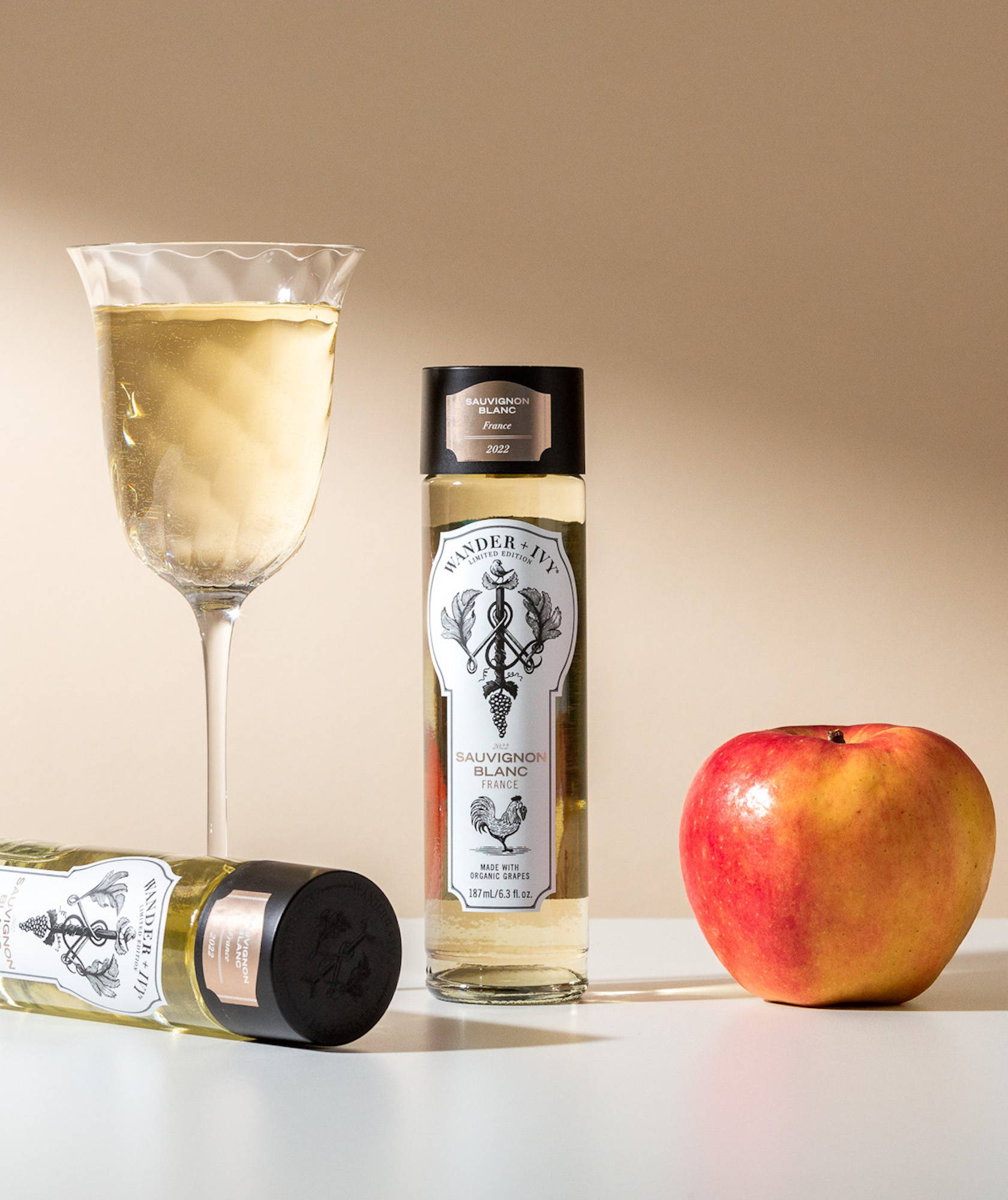 Two single-serve bottles of Sauvignon Blanc next to an apple and a filled wine glass