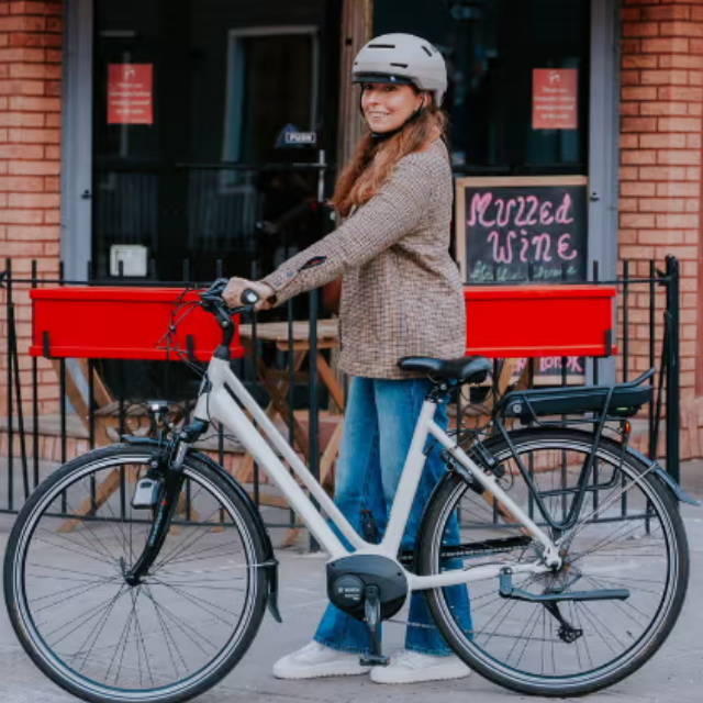 a woman walking her electric bike on the sidewalk in a city