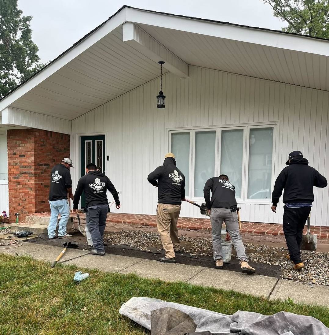 The Hoosier Masonry Solutions crew working on a residential front walkway, preparing the site with gravel and tools in front of a white-paneled home.
