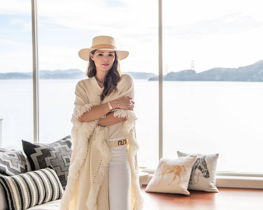 Woman wearing handwoven Long Fringed Alpaca Poncho in  her home filled with sustainable home decor 