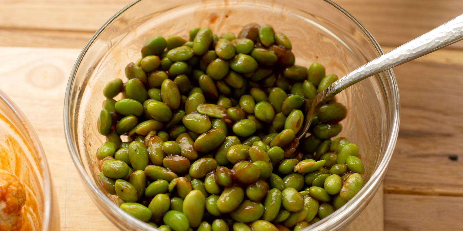 Bowl of edamame coated in bbq sauce with a spoon inside.