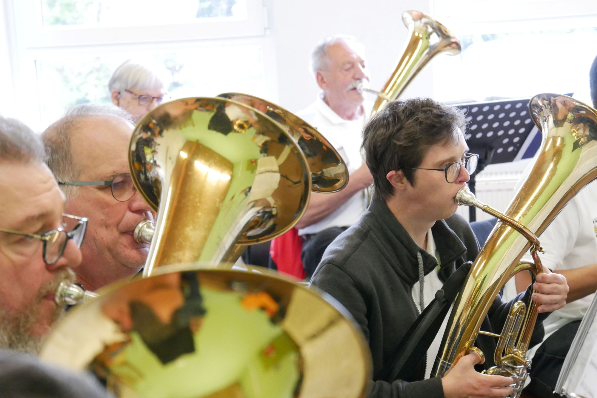 Einige Männer mit und ohne Behinderung sitzen nebeneinander und spielen gemeinsam Tenorhorn. 