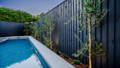 Poolside garden with spike lights highlighting trees along a dark timber fence.