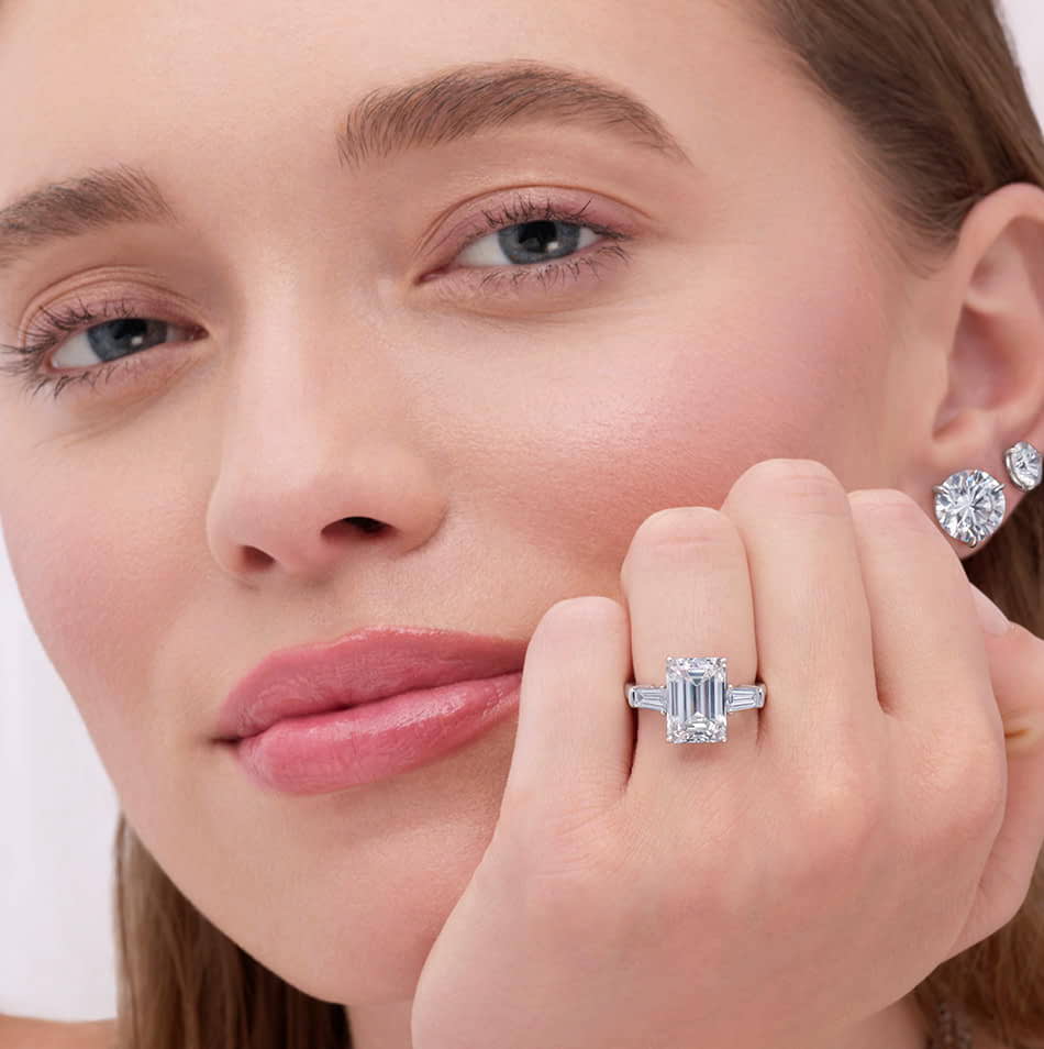 Model wearing a Kwiat emerald cut diamond engagement ring close to her face. 