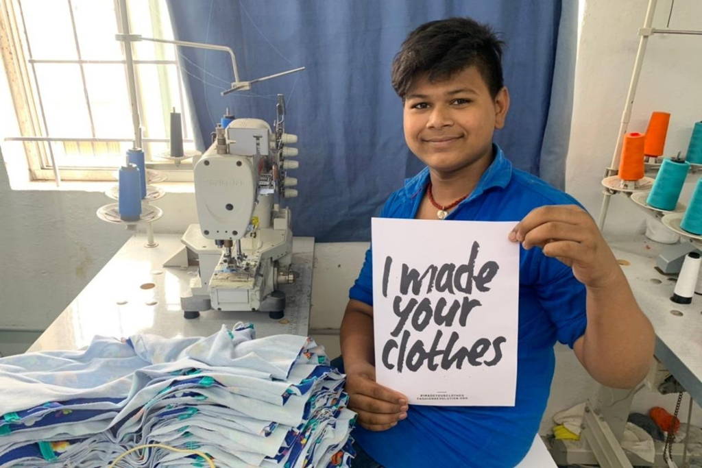 Image of a smiling man in a textile factory holding a sign that says 'I made your clothes'