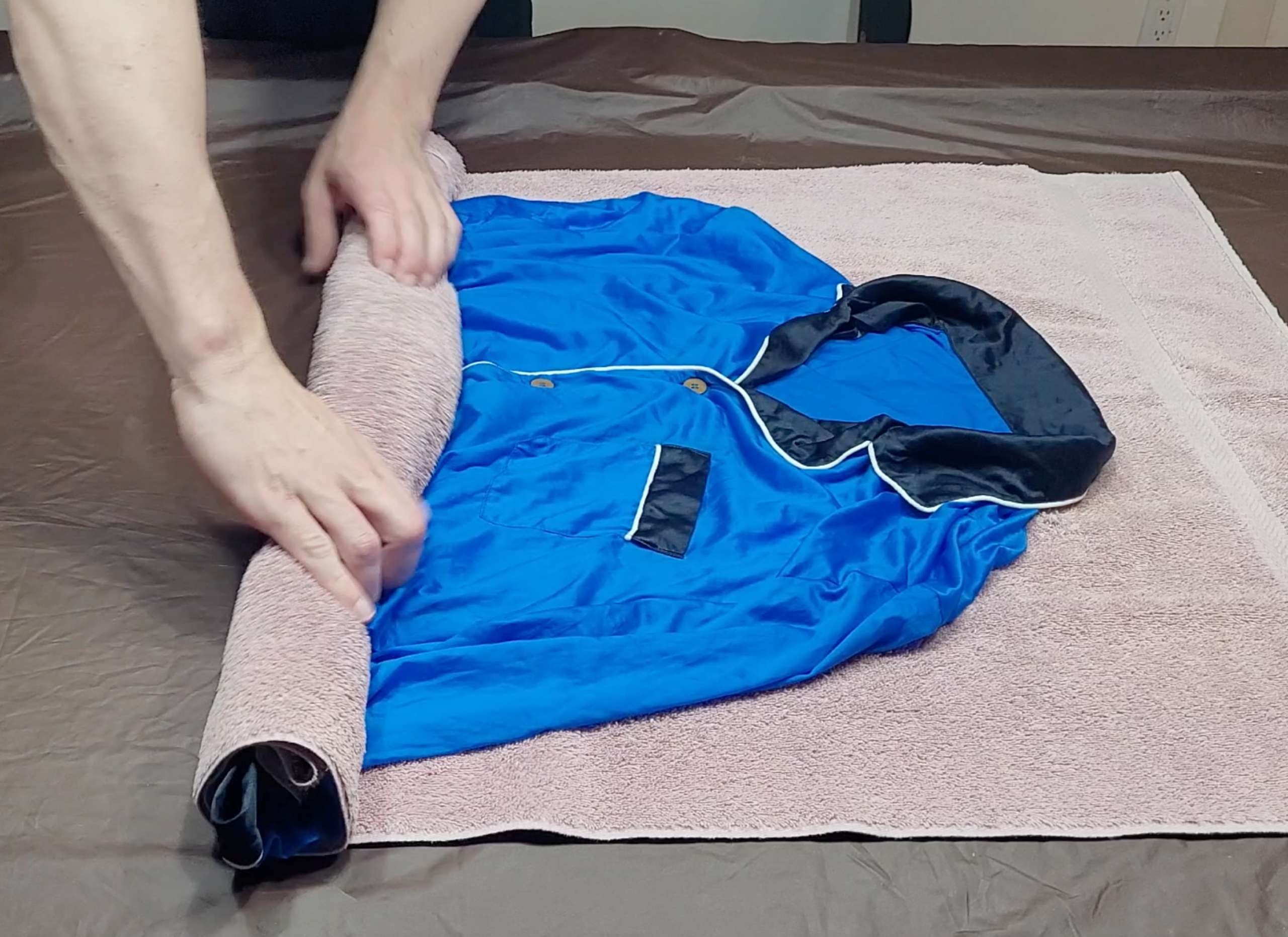 man rolling silk pajamas in a soft towel in order to remove moisture from the silk fabric