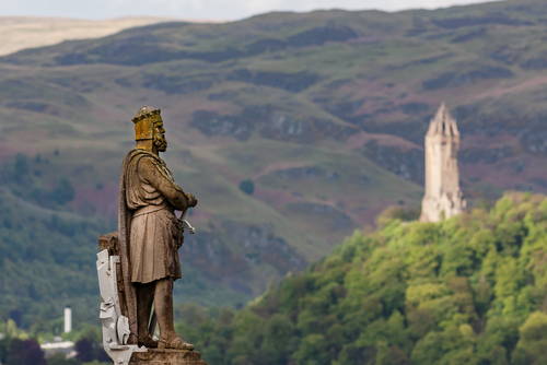 The imposing statue of King Robert The Bruce at Stirling Castle with The Wallace Monument in the distant background on a hill framed by the Ochill Hills