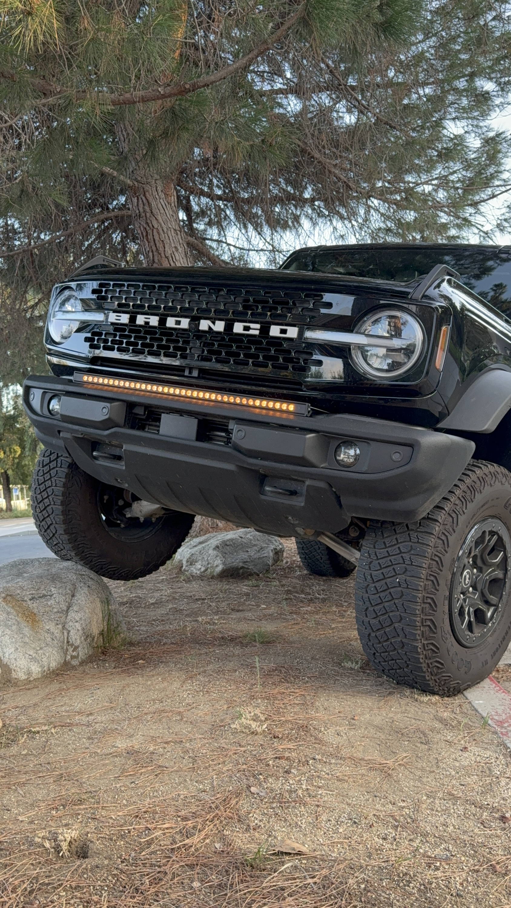black ford bronco standing on top of a rock with amber light bar on top of standard bumper off roading