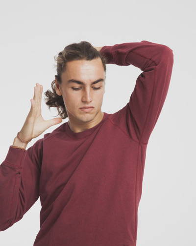 Man wearing burgundy red organic cotton sweatshirt tying up his hair