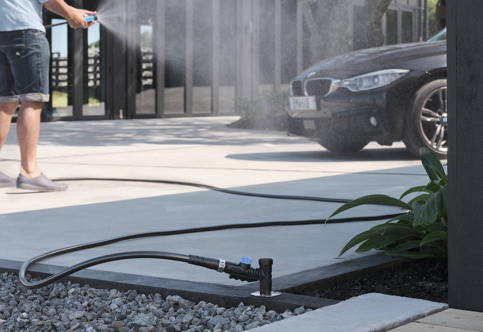 Aquor house hydrant installed in the ground, vacuum breaker connector plugged in, man in background using hose to spray down his car