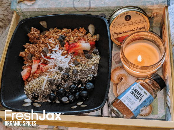 A mother's day parfaits of pleasure gift basket with a bowl of maple cinnamon parfait next to a bottle of FreshJax maple cinnamon topping and lit peppermint bark candle. 