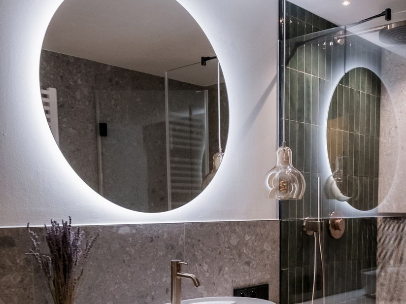 Modernes Badezimmer mit rundem beleuchtetem Spiegel und Dusche im Apartment von Hugo & Pepi im Kleinwalsertal.