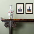 An antique Chinese altar table with scroll ends and framed Chinese pith paintings hung in a living room
