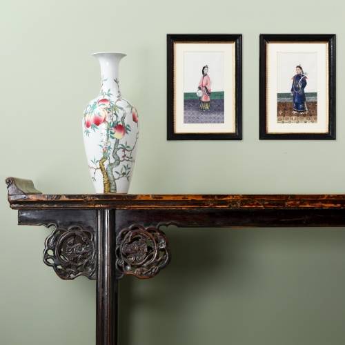 An antique Chinese altar table with scroll ends and framed Chinese pith paintings hung in a living room