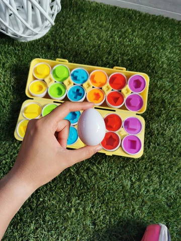 A hand holding an egg with colorful Montessori Geometric Eggs in the background.