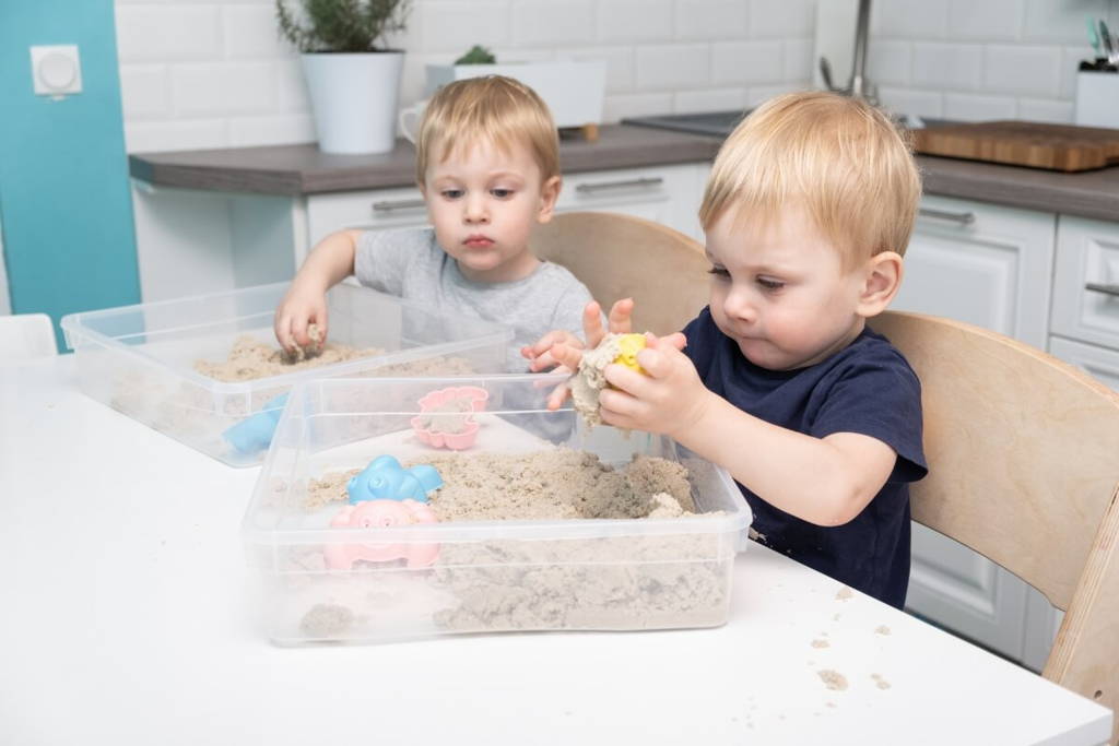 Two little boys playing with make dough in plastic sensory bins.