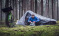 Un cycliste à l’entrée de sa tente, son vélo équipé pour le bikepacking à côté