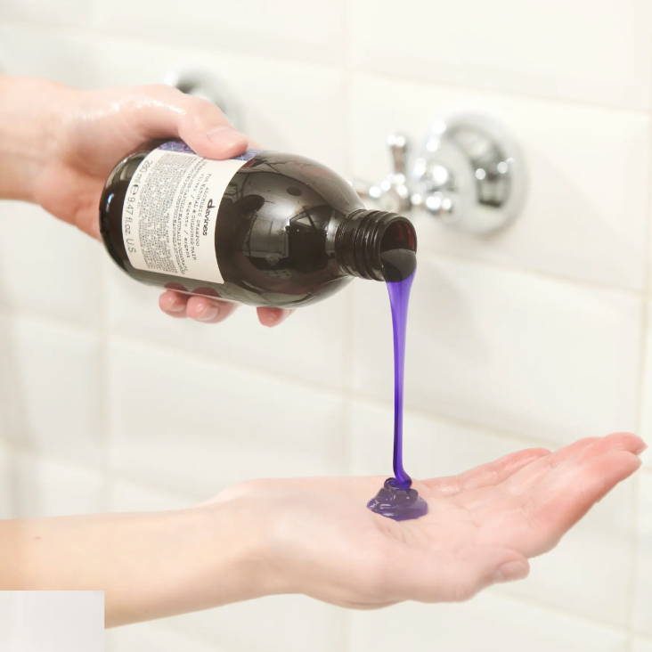 hands pouring Davines Alchemic Silver shampoo, blue shampoo is dripping out