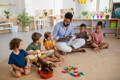 A Montessori teacher playing musical instruments with children in a playroom.