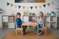 Kids sitting on a table in their playroom and smiling. 