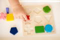 Baby's hand placing a red star puzzle on the wooden Montessori board. 