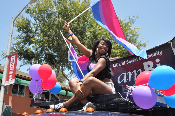 A black woman sits on the amBi parade float smiling waving the flag.
