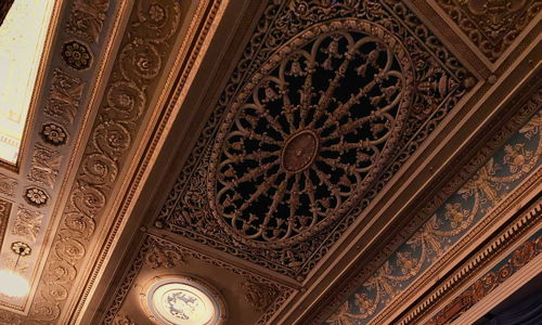 Interior of a theater featuring an ornate ceiling, rich purple curtain, elegant details, and a dramatic ambiance.