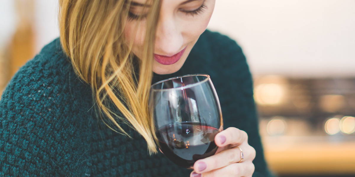 Woman smelling a glass of red wine highlighting the notion of smell while tasting wine.