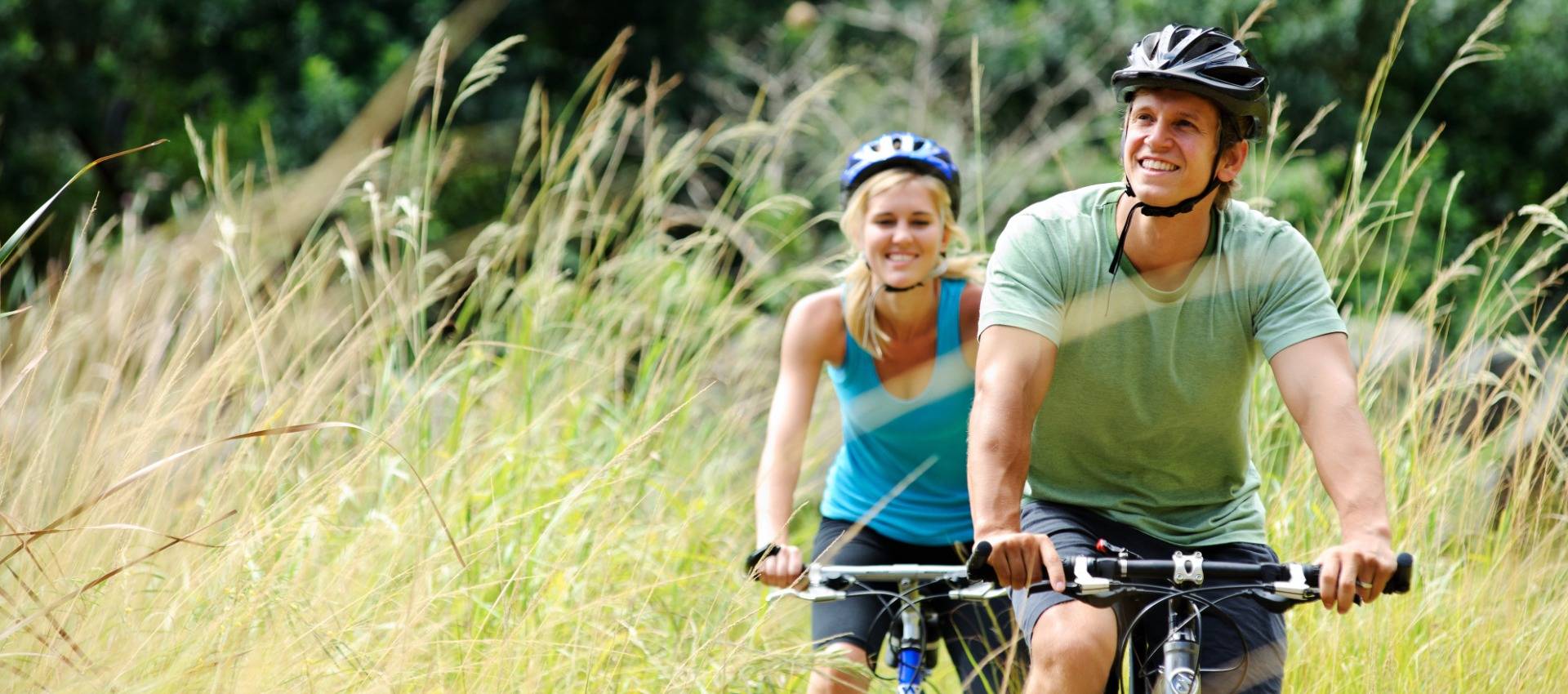 Ein Mann und eine Frau fahren gemeinsam Fahrrad durch hohes Gras