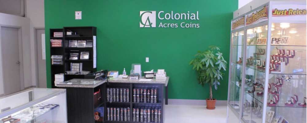 Interior of Colonial Acres Coins shop showing a green feature wall with company logo, service counter, and glass display cases