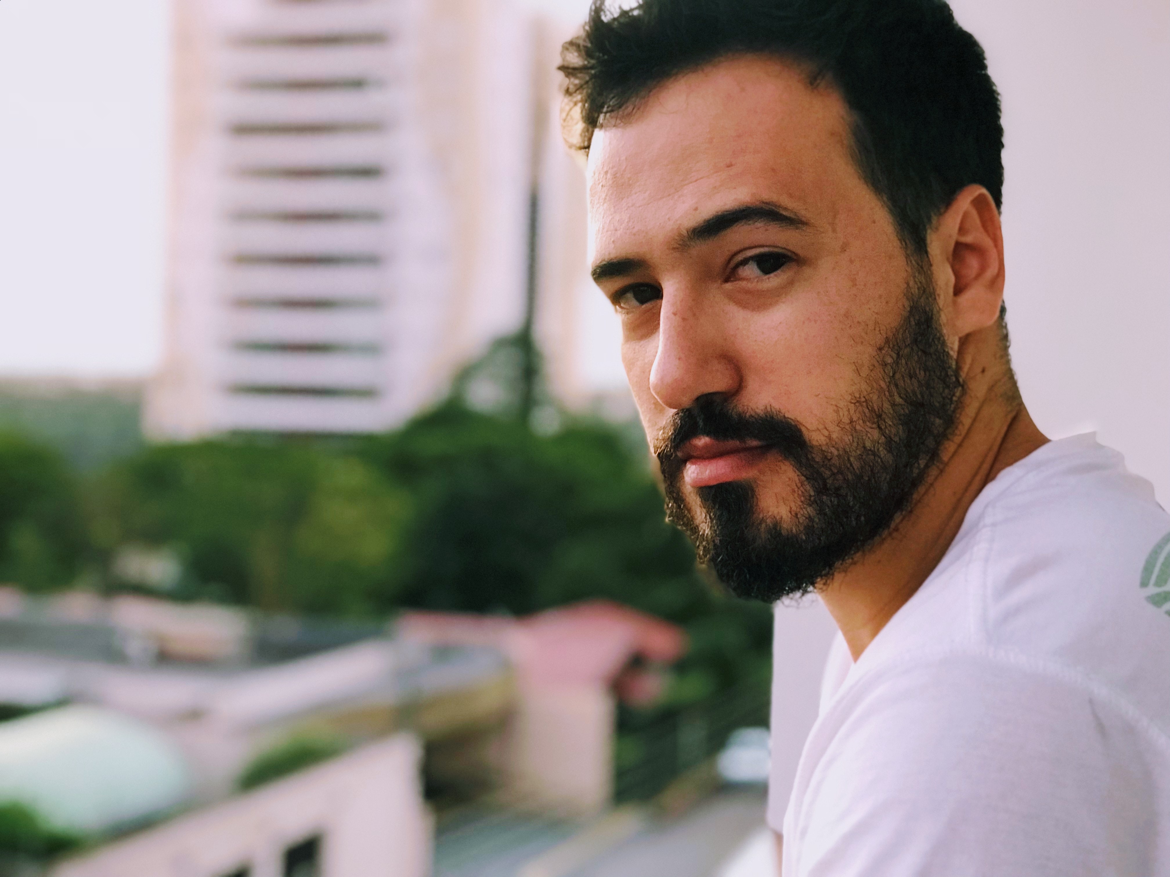 A man smirks while standing on a balcony looking to his side to the camera.