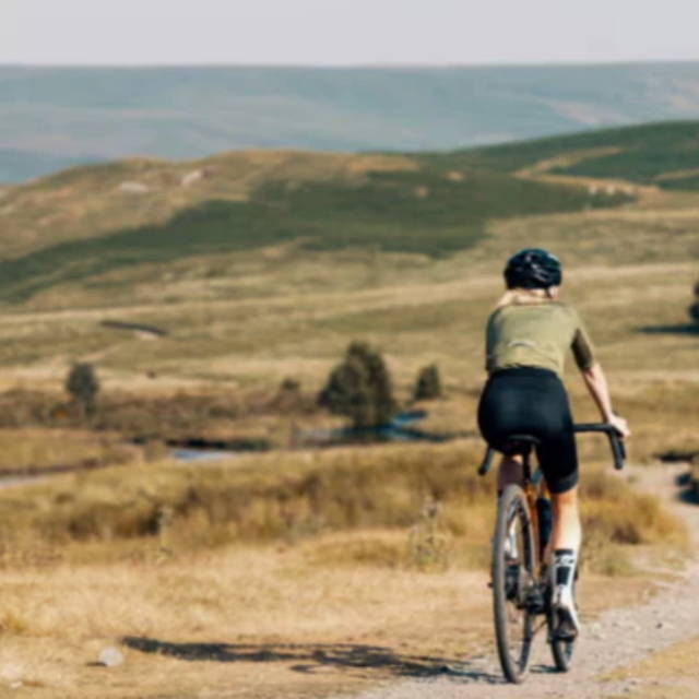 a woman riding a gravel bike over trail surrounded by tan grass