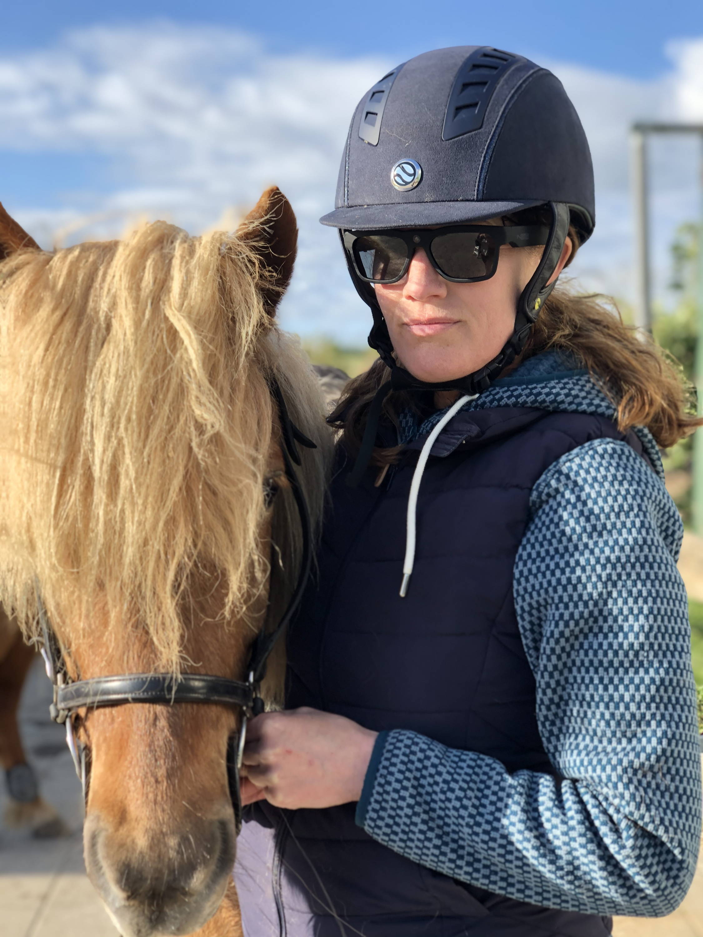 Camilla Jørgensen står med kamera solbriller på sammen med sin hest efter ridning.