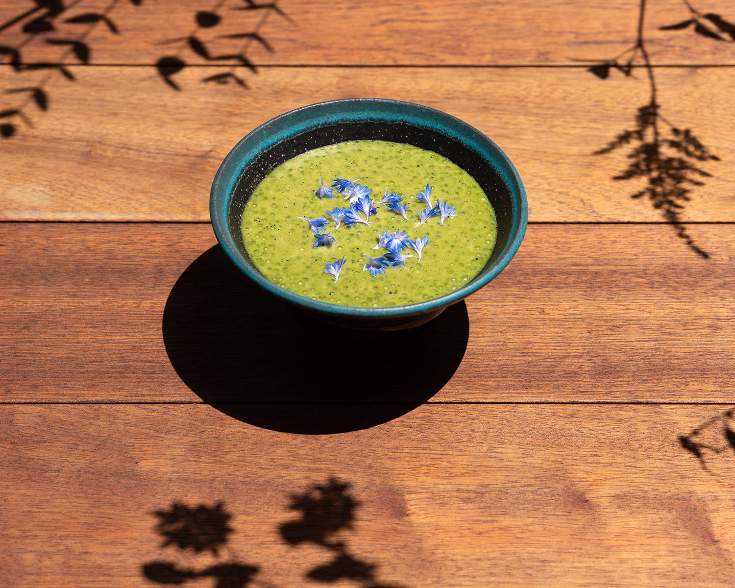 A bowl of jade-colored matcha tapioca, garnished with purple flowers.