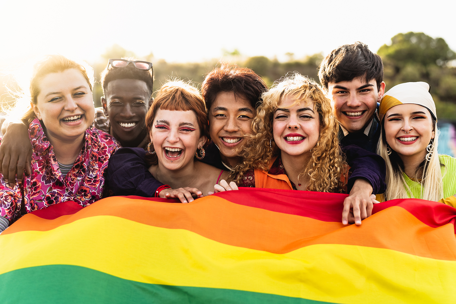 A diverse young friends celebrating gay pride festival holding a pride flag together