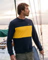 Man wearing navy and yellow organic cotton sweatshirt standing on a boat, with clothing from Cornish sustainable outdoor clothing brand, Finisterre