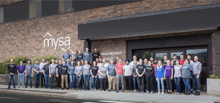 group of Mysa employees wearing branded shirts standing outside of their office building