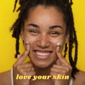 Model smiling, with index fingers on her cheeks which have two dots of Clear Skin Days Blemish Repair Paste