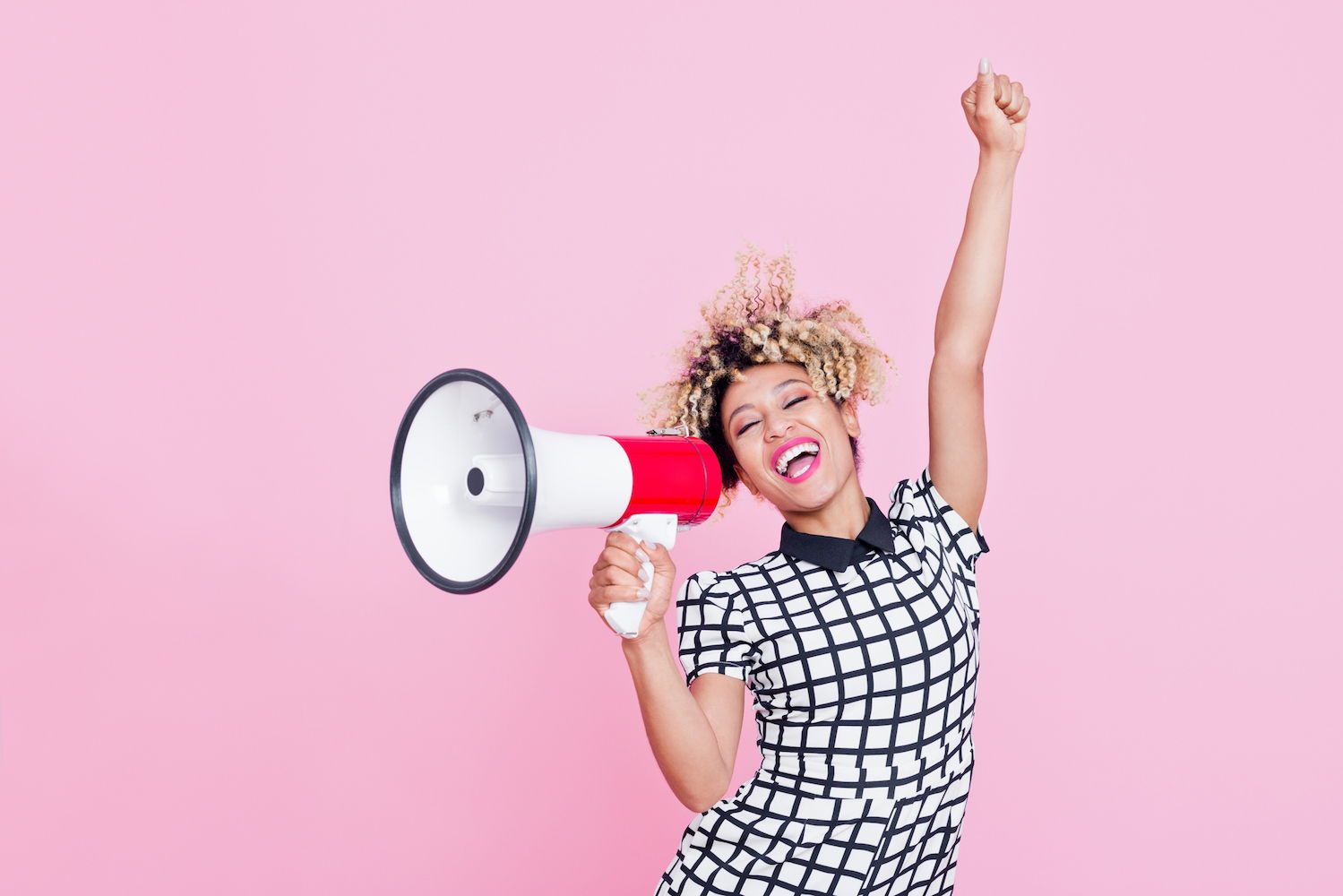 A woman holds her hand in the air and speaks into a megaphone with a smile.