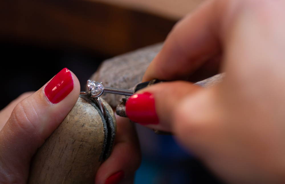 Jewelers' hands work on an engagement ring on a jeweler's bench.