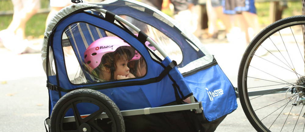 Two kids with pink helmets in bicycle trailler