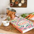 A cookbook titled 'EAST' with a floral background sits on a wooden cutting board next to cardamom pods & a mortar and pestle