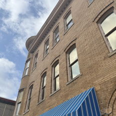 A charming brick building with large windows and a bright blue awning, evoking warmth and nostalgia under a partly cloudy sky.