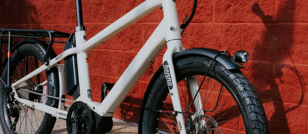 a white Benno Boost electric cargo bike against a red brick wall